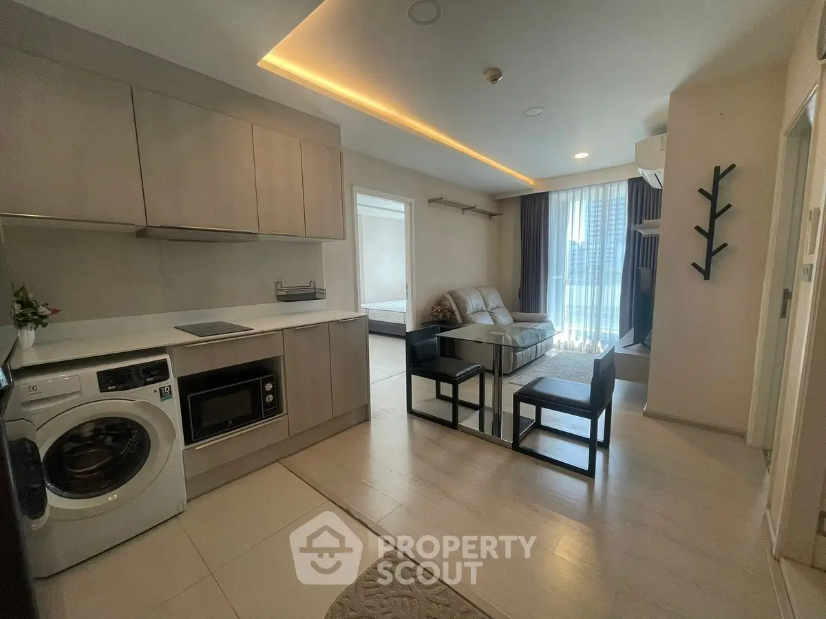 Modern open-layout apartment with sleek kitchen and cozy living area, featuring a washing machine and ample natural light.