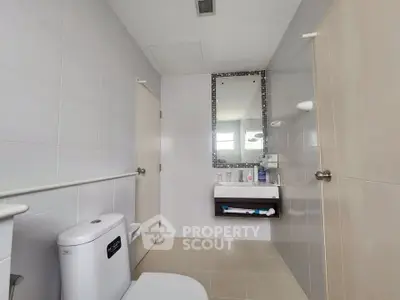 Modern bathroom with sleek fixtures and neutral tiles, featuring a large mirror and compact vanity.
