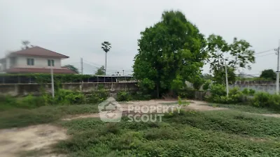 Vacant land with lush greenery and distant house, ideal for development.
