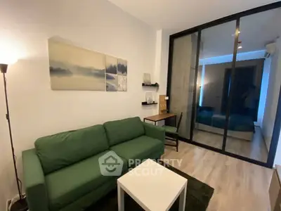 Modern living room with green sofa, stylish decor, and sliding glass doors leading to bedroom.