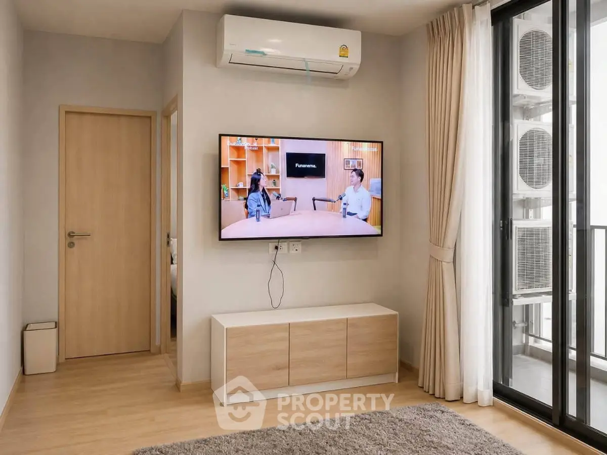 Modern living room with air conditioning and balcony access, featuring a mounted TV and sleek furniture.