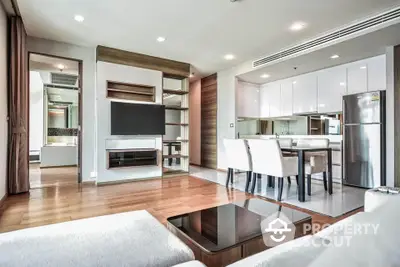 Modern open-plan living room with sleek kitchen and dining area, featuring contemporary furniture and wooden flooring.