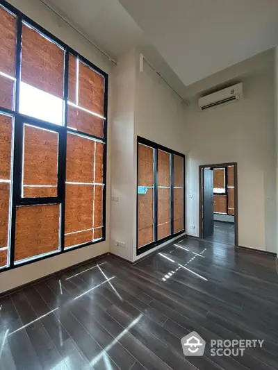 Spacious modern room with high ceilings and large windows featuring wooden blinds.