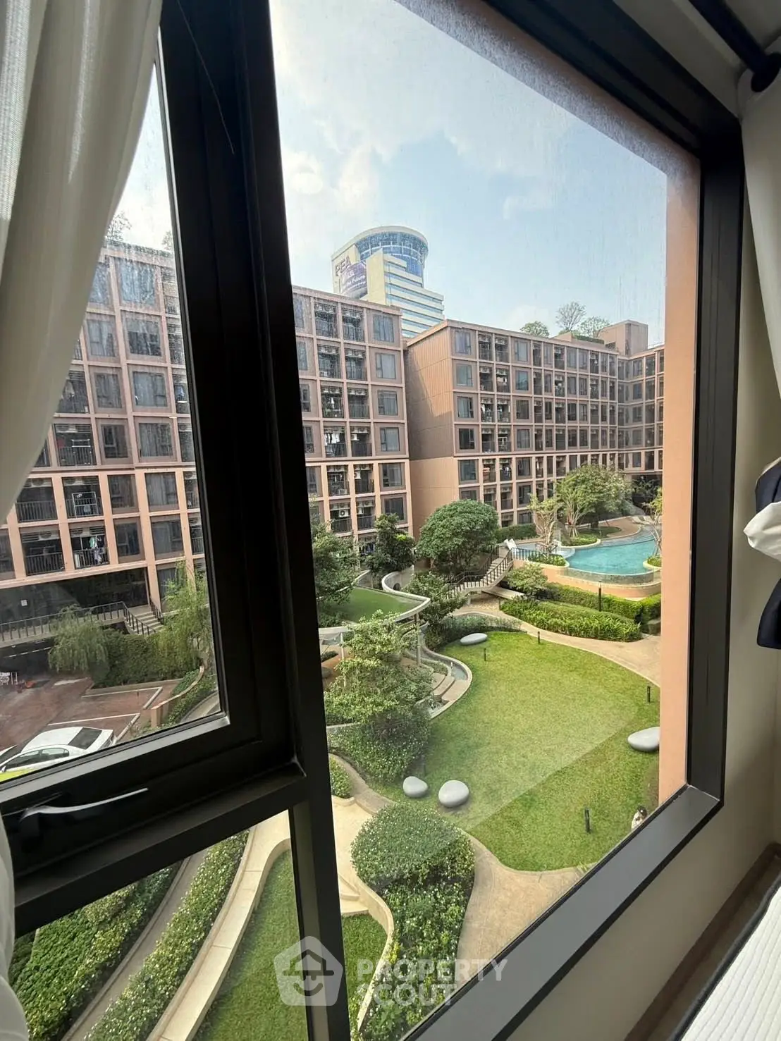 Stunning view from window overlooking lush garden and pool in modern apartment complex.