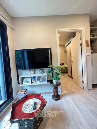 Modern living room with stylish decor and large TV, featuring light wood flooring and elegant furnishings.