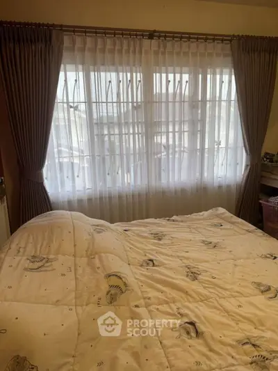 Cozy bedroom with large window and elegant curtains, inviting natural light.