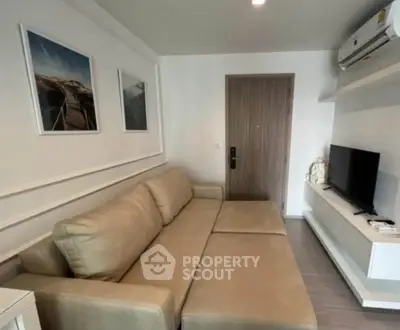 Modern living room with beige sofa, wall-mounted TV, and air conditioning unit.