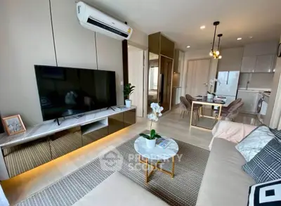 Modern living room with sleek furniture and open dining area, featuring a large TV and stylish decor.