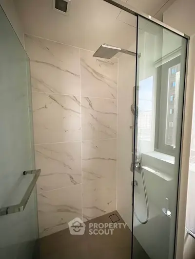 Modern bathroom with glass shower and marble tiles, featuring sleek fixtures and natural light.