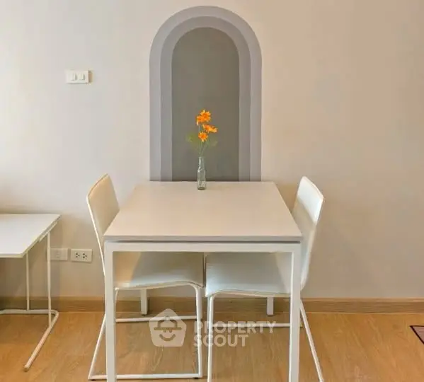 Modern minimalist dining area with sleek white table and chairs, accented by a decorative wall niche.
