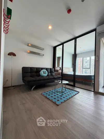 Modern living room with sleek design and glass partition leading to bedroom, featuring stylish decor and natural light.