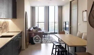 Modern living room with open kitchen, stylish decor, and large windows offering natural light.