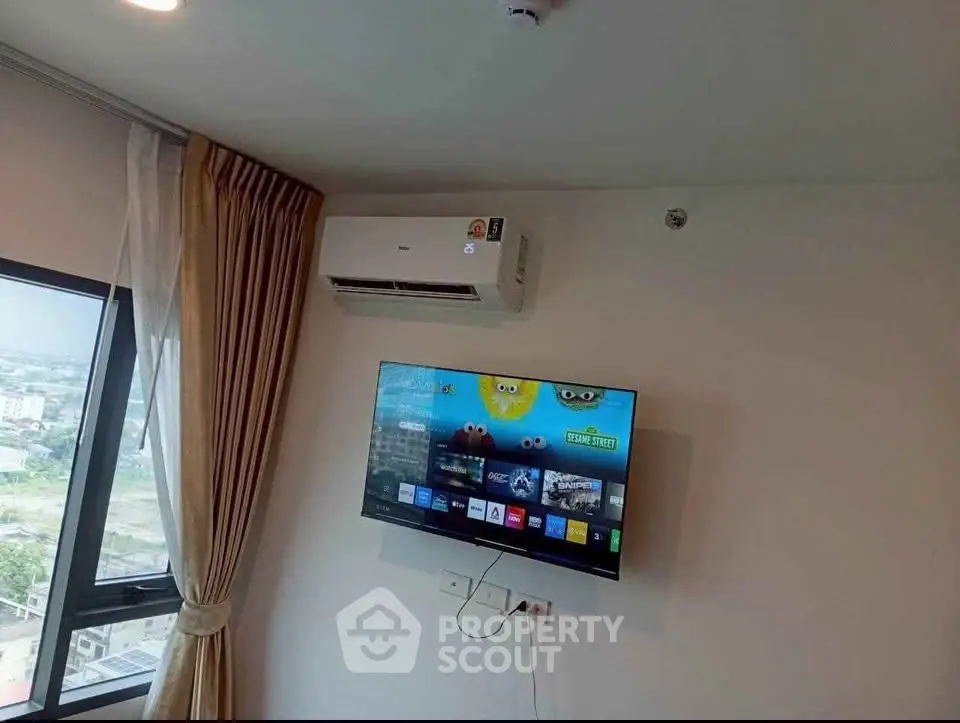 Modern living room with wall-mounted TV and air conditioning, featuring large window with city view.