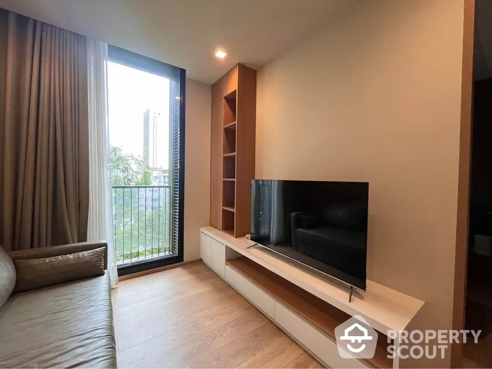 Modern living room with sleek furnishings and abundant natural light streaming in from floor-to-ceiling glass door leading to a balcony.