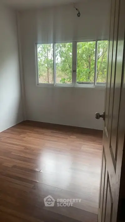 Spacious empty room with large window and wooden flooring, perfect for customization.