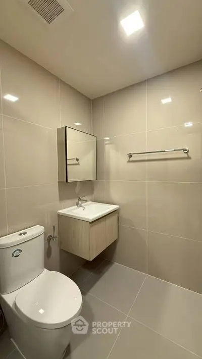 Modern bathroom with sleek fixtures and neutral tiles, featuring a wall-mounted sink and toilet.
