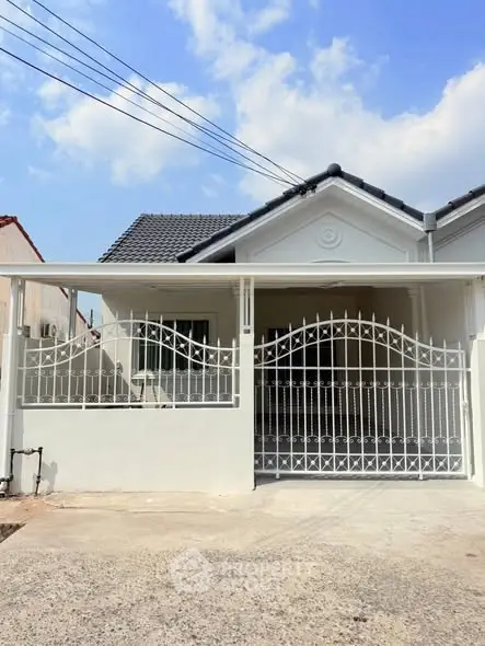 Charming single-story house with gated entrance and modern roof design under a clear blue sky.