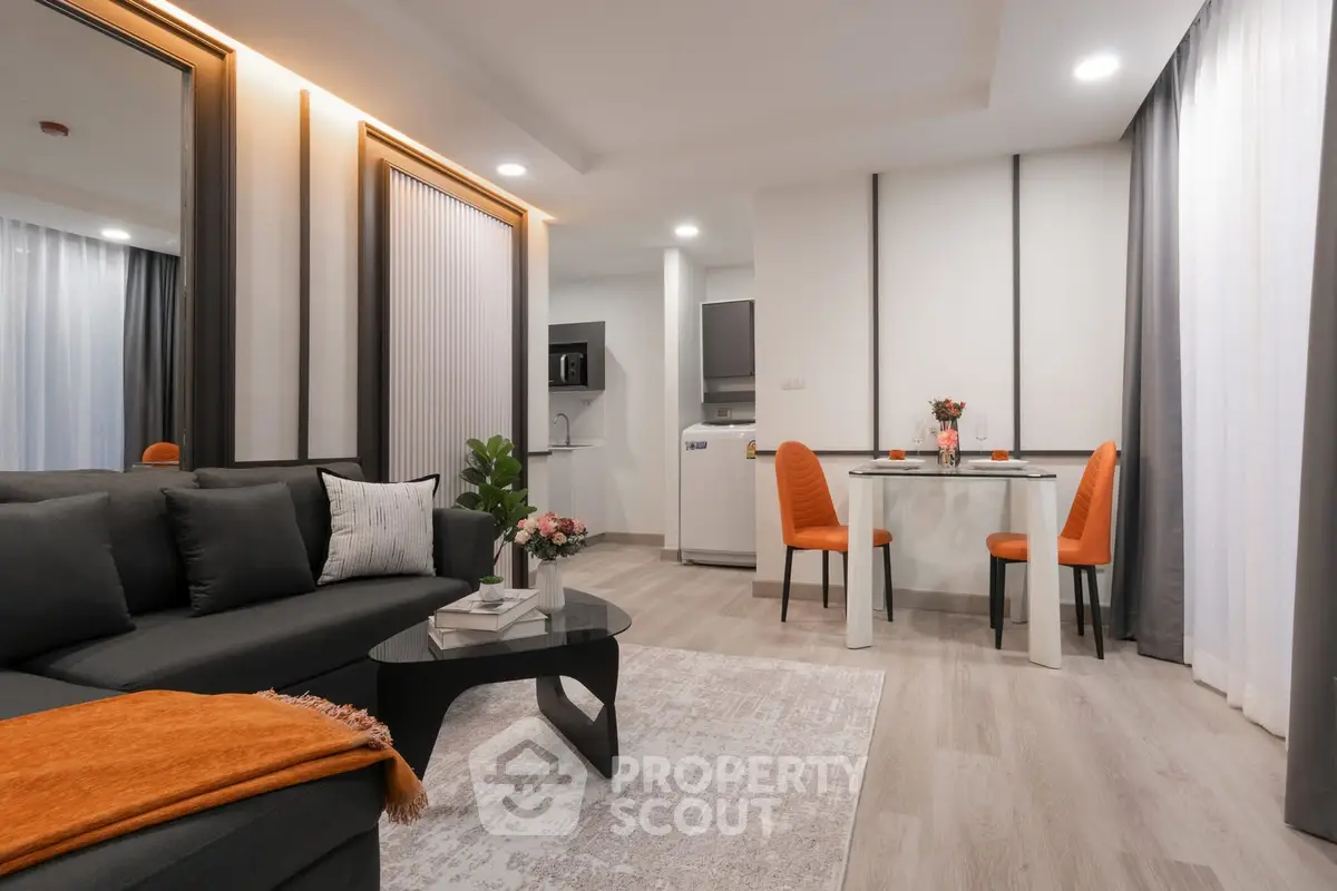 Modern living room with stylish decor and open kitchen layout, featuring sleek furniture and warm lighting.