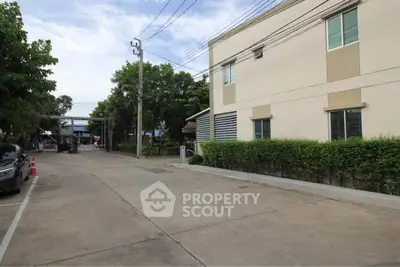 Modern building exterior with lush greenery and spacious driveway in a serene neighborhood.