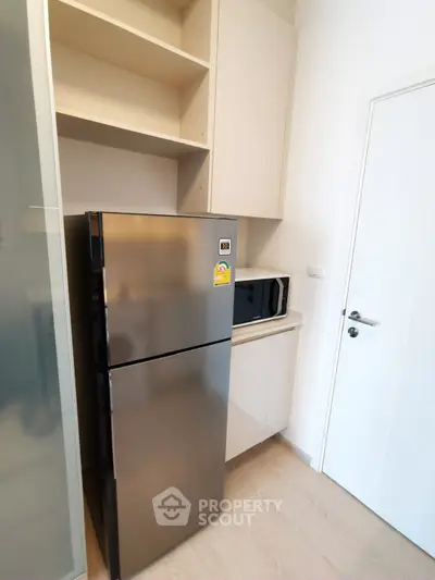 Modern kitchen corner with stainless steel fridge and microwave in sleek cabinetry.