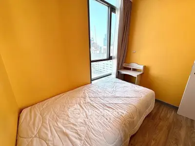 Cozy bedroom with vibrant yellow walls and city view, featuring a comfortable bed and small desk.