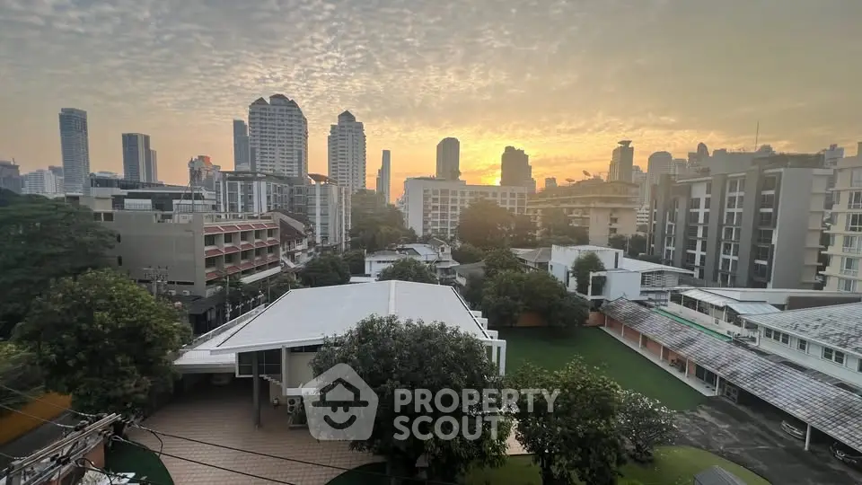 Stunning cityscape view from a high-rise building at sunset, showcasing urban skyline and lush greenery.