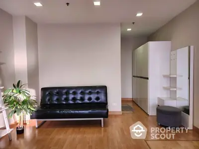 Spacious living room with polished hardwood floors, modern black leather sofa, and sleek white shelving units, complemented by ambient lighting.