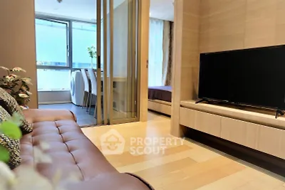 Modern living room with sleek TV and cozy seating, leading to a bright dining area and bedroom.