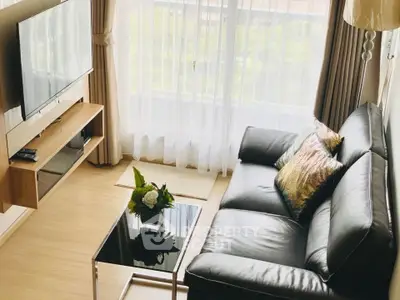 Modern living room with sleek black sofa, wall-mounted TV, and large window with sheer curtains.