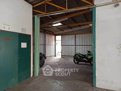 Spacious industrial warehouse with high ceiling and ample storage space, featuring secure metal doors and motorcycle parking.