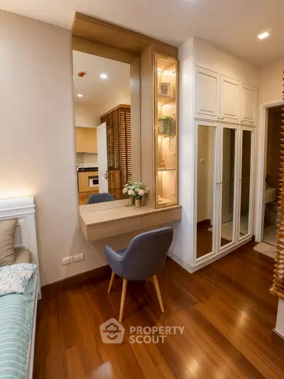 Chic bedroom with elegant vanity and cozy seating, featuring warm wooden flooring and stylish decor.