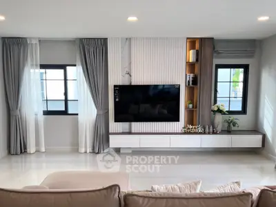 Modern living room with sleek TV setup and elegant decor, featuring large windows and stylish curtains.