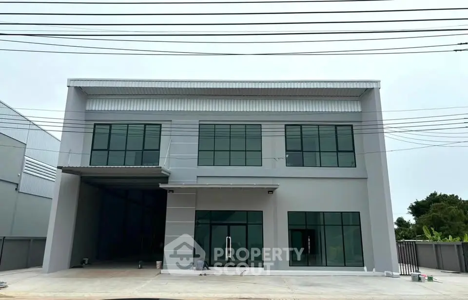 Modern industrial building with large glass windows and spacious parking area.