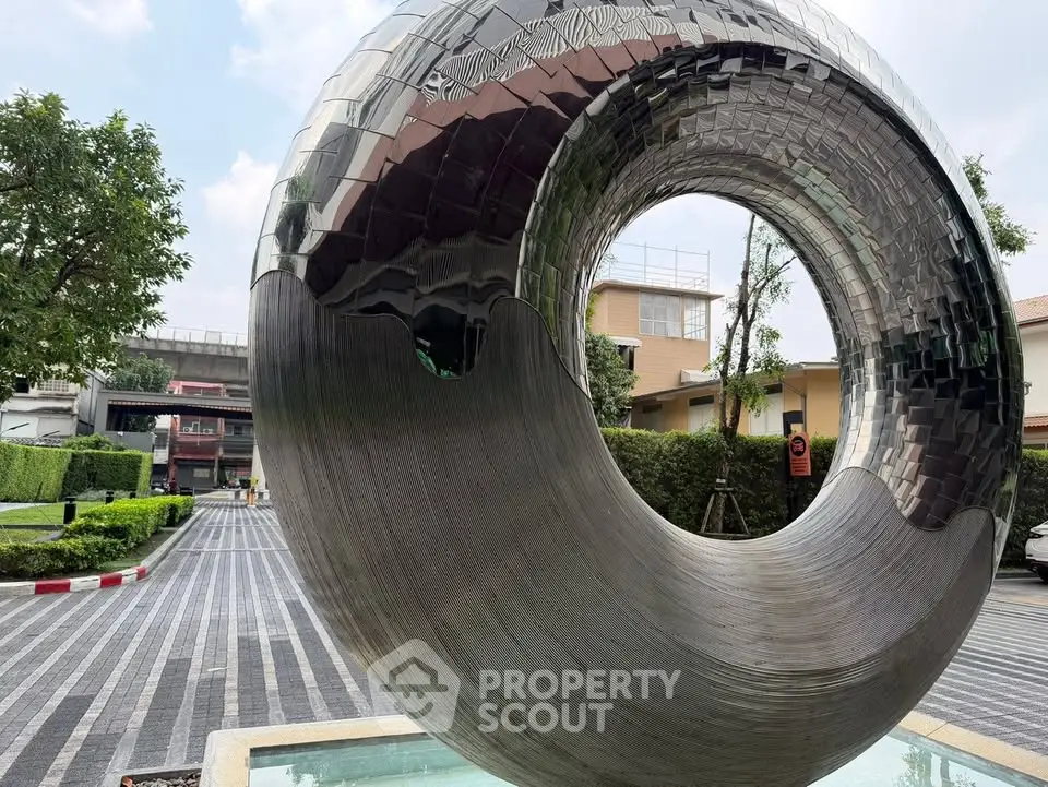 Modern sculpture in upscale residential area with lush greenery and stylish architecture.
