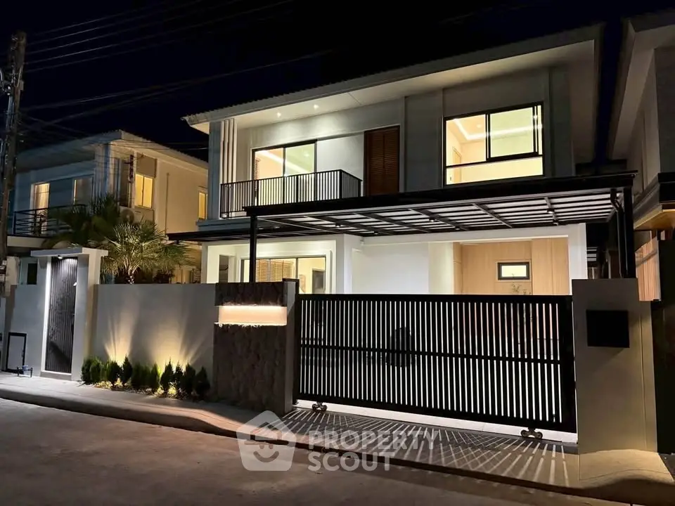Modern two-story house with sleek design and illuminated facade at night, featuring large windows and gated entrance.