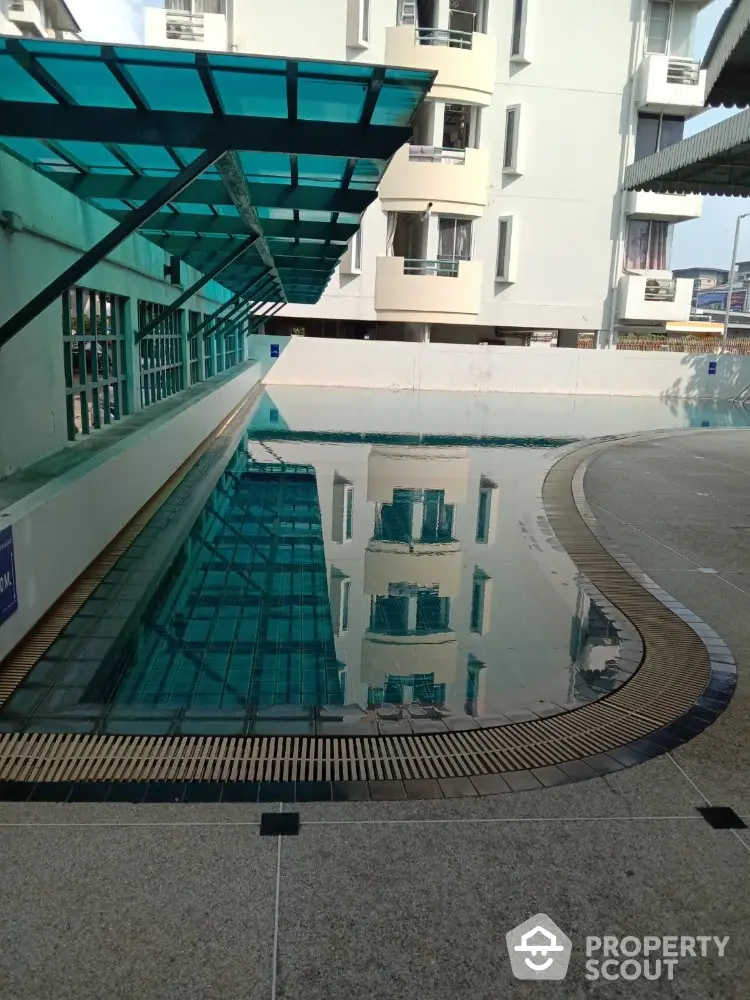 Modern apartment building with a sleek swimming pool and glass canopy, perfect for urban living.