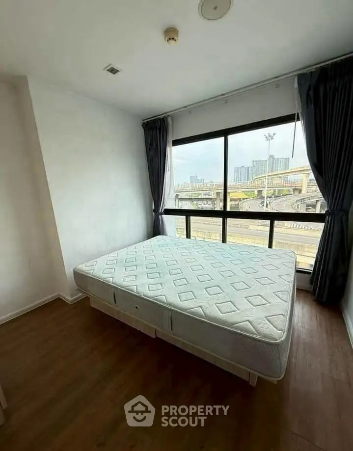 Spacious bedroom with large window offering city view, featuring a comfortable bed and elegant curtains.