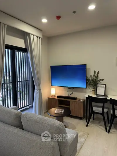 Modern living room with sleek decor, large TV, and natural light from window.