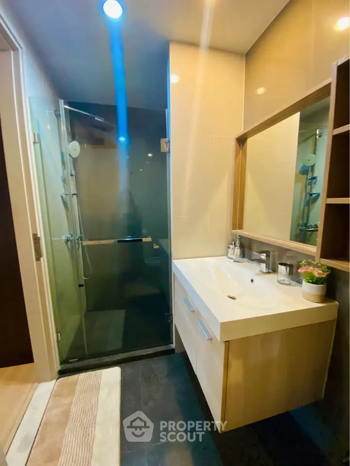 Modern bathroom with glass shower and sleek vanity in contemporary apartment.