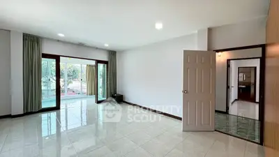 Spacious living room with large windows and tiled flooring, offering ample natural light and a serene view.