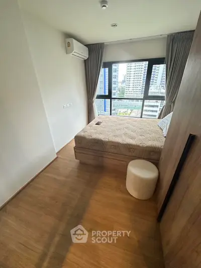 Modern bedroom with large window and city view, featuring cozy bed and wooden flooring.