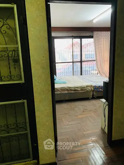 Cozy bedroom with large windows and parquet flooring, offering natural light and comfort.