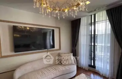 Elegant living room with modern chandelier and large TV, featuring a cozy curved sofa and floor-to-ceiling windows.