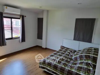 Spacious bedroom with wooden flooring and large window offering natural light.