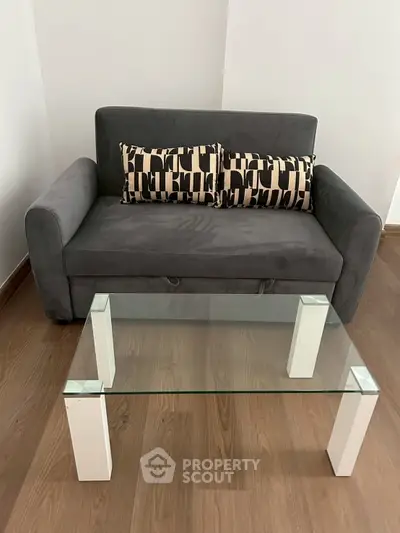 Modern living room with stylish gray sofa and glass coffee table on wooden floor.