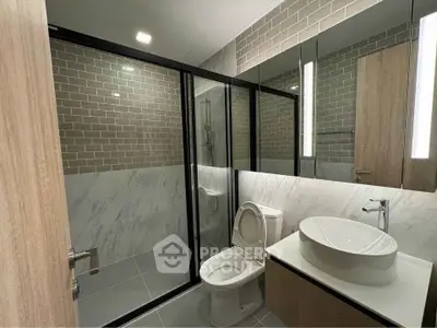 Modern bathroom with glass shower, stylish sink, and elegant tile design.