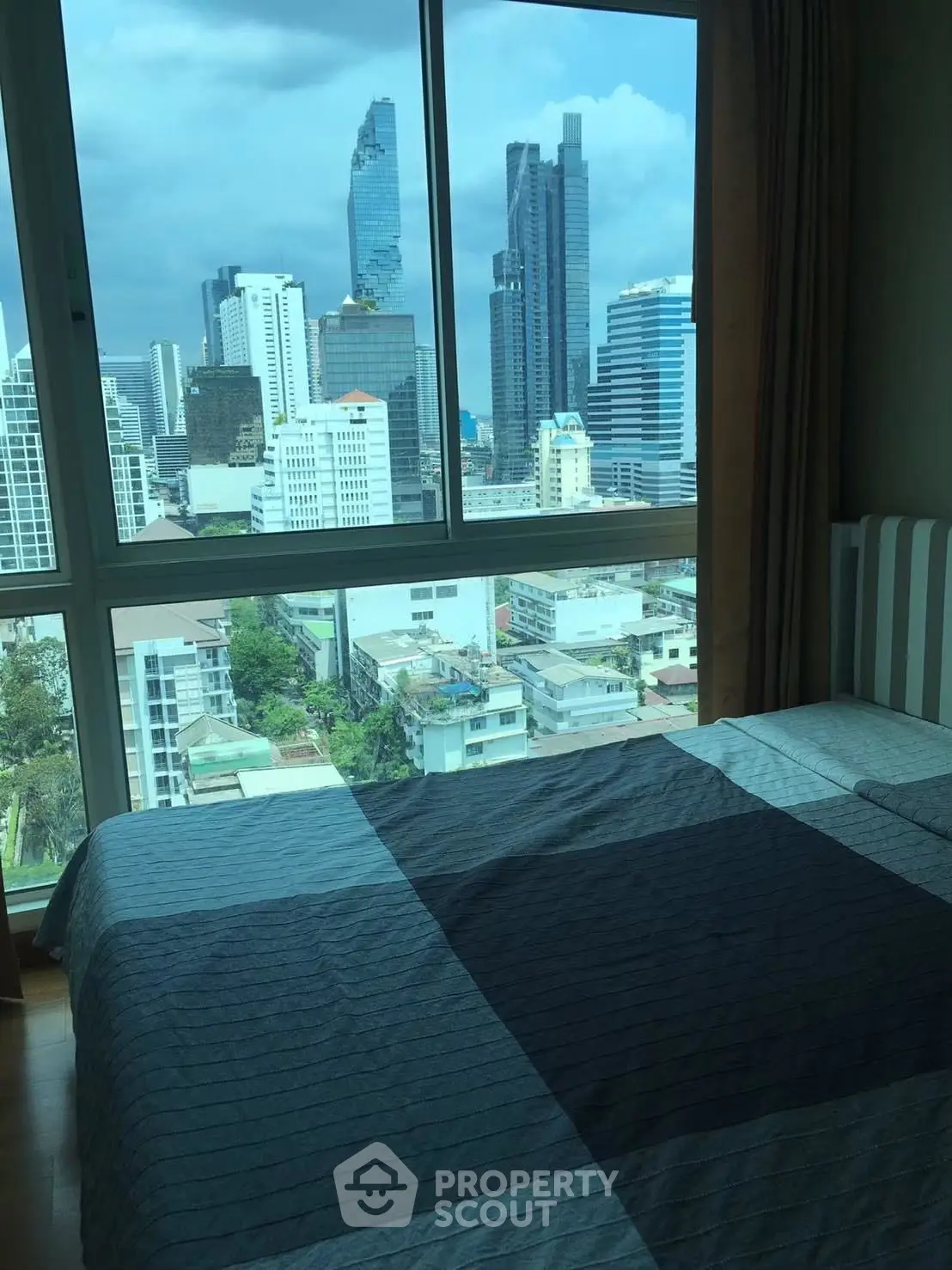 Stunning city view from a modern bedroom with large windows and cozy bedding.