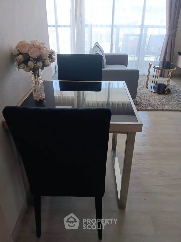 Modern living room with glass dining table and cozy seating area, featuring elegant decor and natural light.