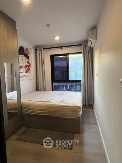 Modern bedroom with large window and stylish decor in urban apartment.