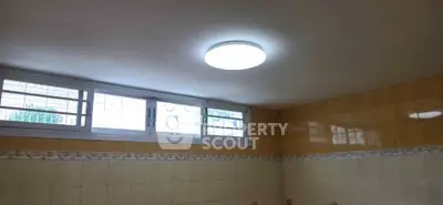 Bright bathroom with tiled walls and ceiling light, featuring small windows for natural light.